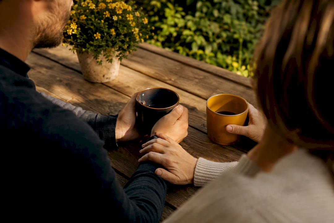 Hand touching wrist over coffee mugs symbolizing trust repair